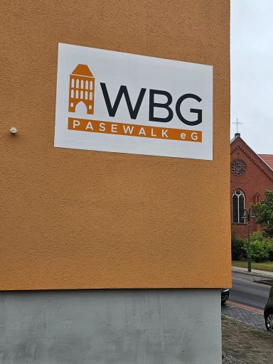 WBG Passau, Logo auf einer orangefarbenen Wand, im Hintergrund eine Kirche.